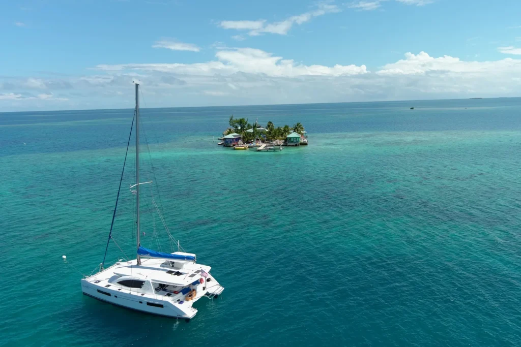 A Belizean catamaran gracefully sails past a secluded island during unforgettable oceanic getaways with Belize Sailing Vacations.