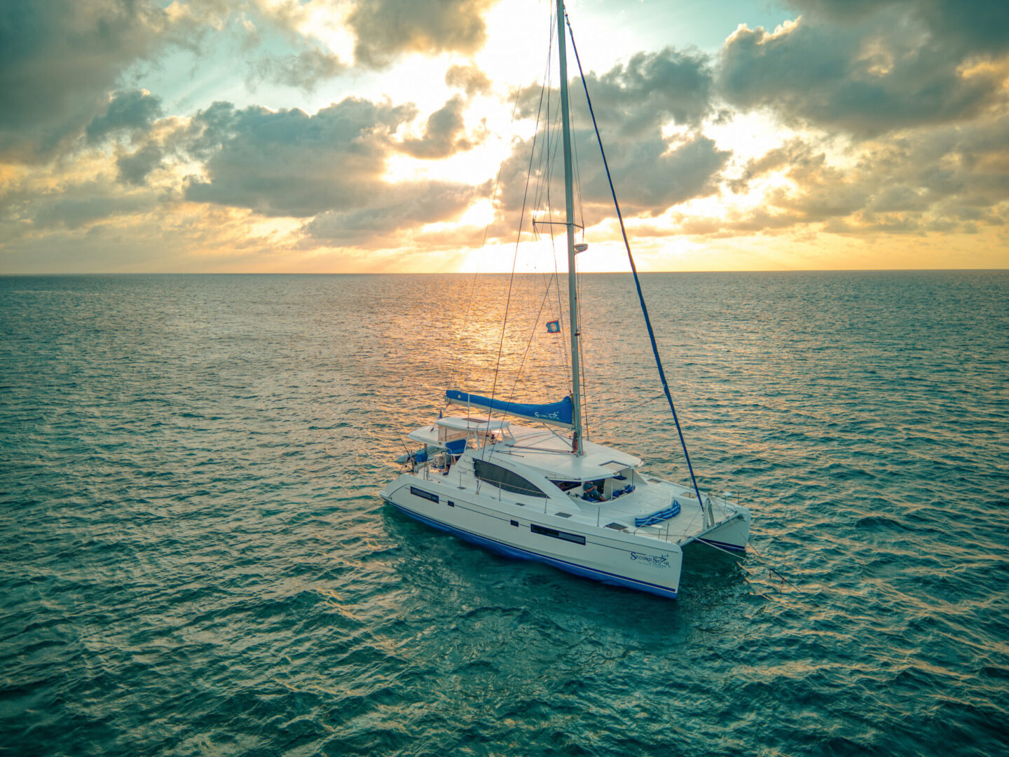 A catamaran sails in the ocean during a Belize Sailing Vacation at sunset.