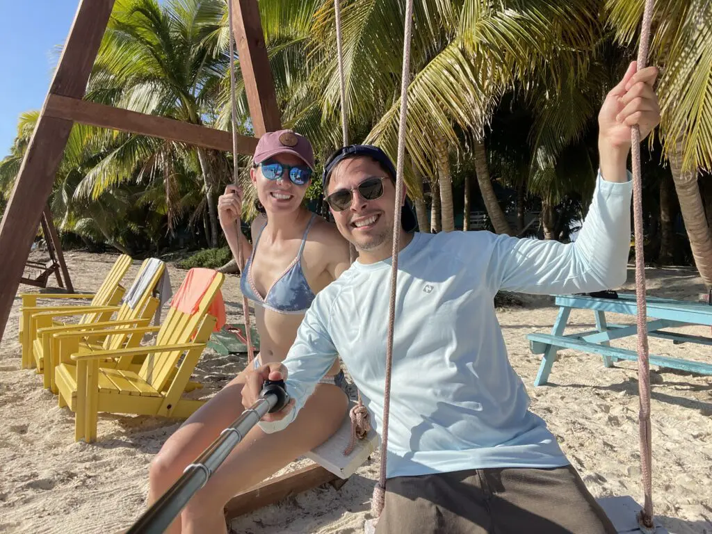 A man and woman enjoying a Belize sailing vacation on a swing on the beach.