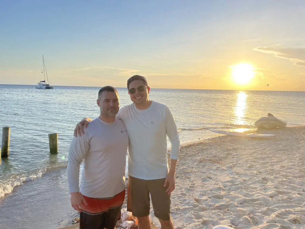 Two men enjoying a Belize vacation at sunset on the beach.