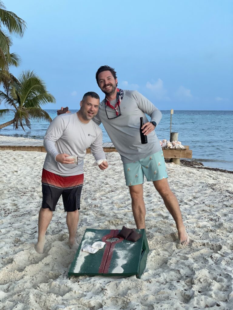 Two men posing next to a Christmas box on the beach during their Belize vacation.
