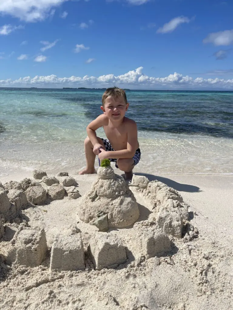 A young boy enjoying a Belize beach vacation, building a sand castle on the shore.