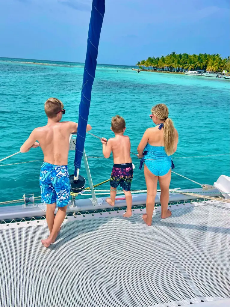 Three children standing on the deck of a catamaran.