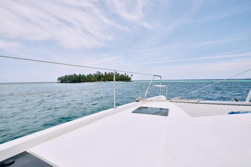 Experience a memorable Belize sailing vacation, as you relax on the deck of a boat with a picturesque small island in the background.