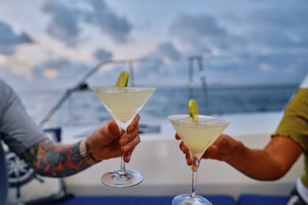 Two people enjoying Belize Sailing Vacations on a boat, toasting martinis during the tour.