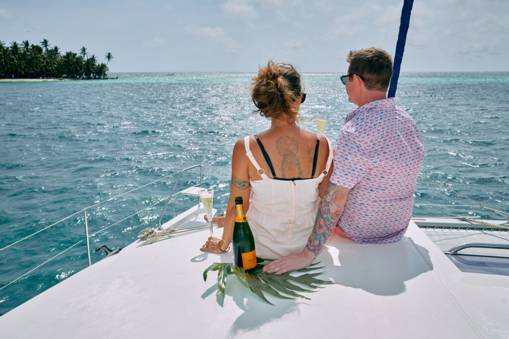 A couple on a Belize Sailing Vacation, sitting on a boat in the ocean with a bottle of champagne.