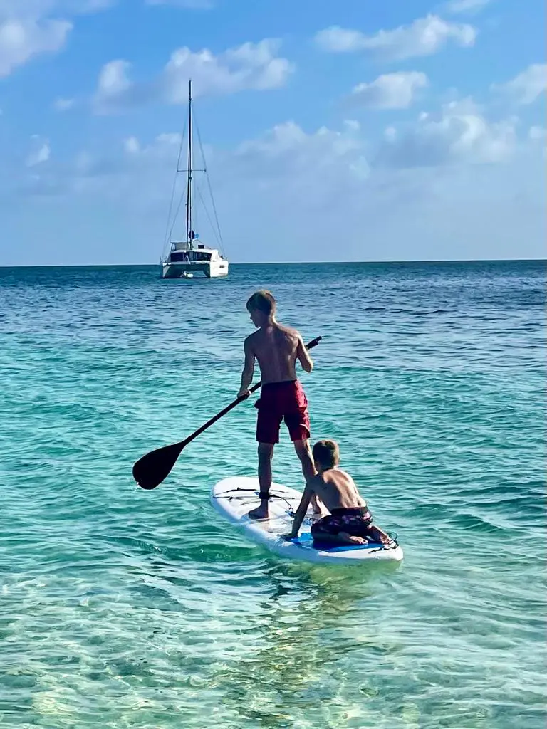 Two people enjoy Belize Sailing Vacations while stand up paddle boarding in the clear blue water.