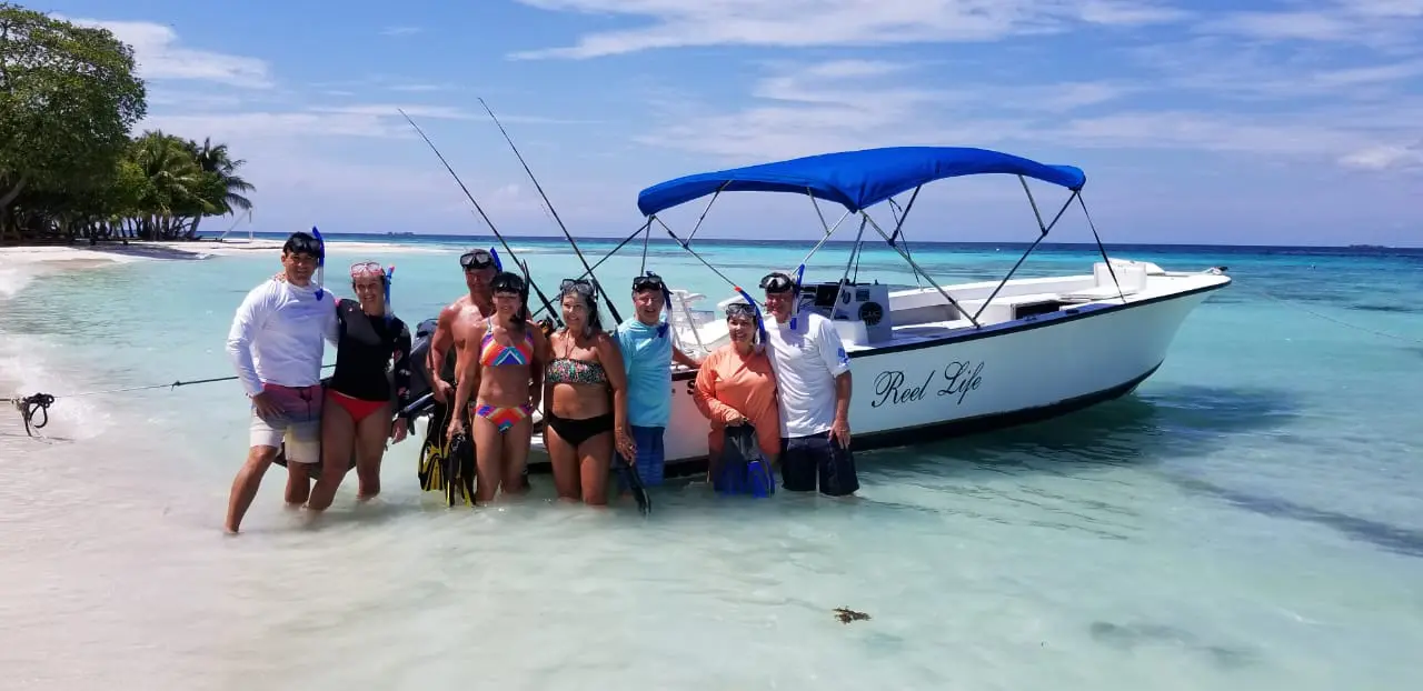 A group of people posing in front of a boat during a Belize Sailing Tour.