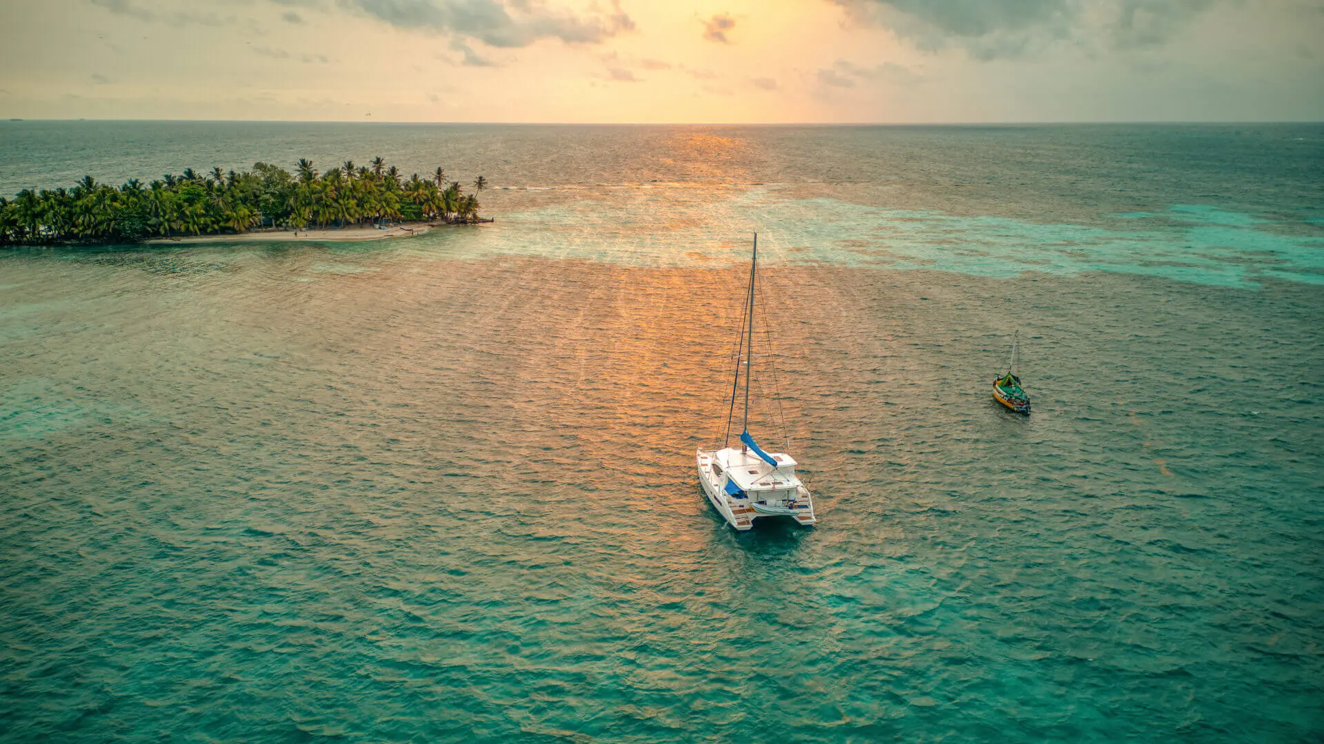 An aerial view of a sailboat in the ocean near an island on a vacation.