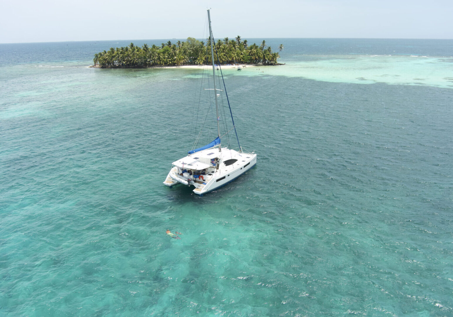 A white sailboat is floating in the water near a small island, offering a picturesque scene for Belize Sailing Vacations and Tours.